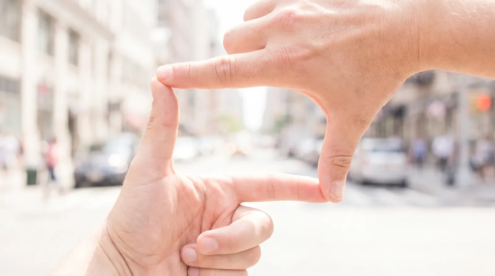 Two hands forming a rectangular frame against a blurred city street